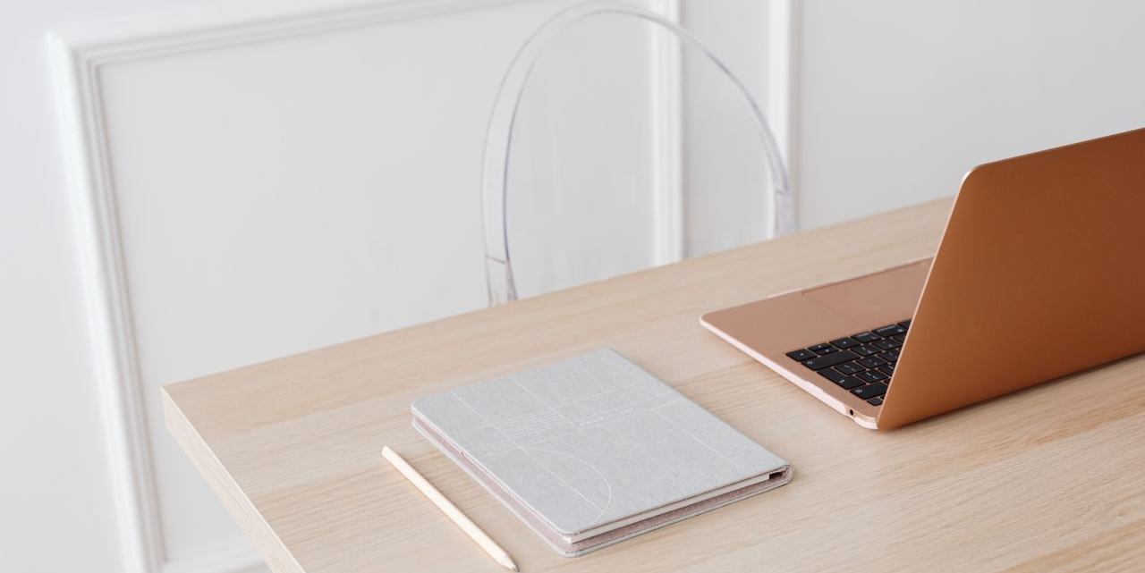 Een rustige werkplek met een laptop, een notitieboek en een potlood op een houten tafel.
