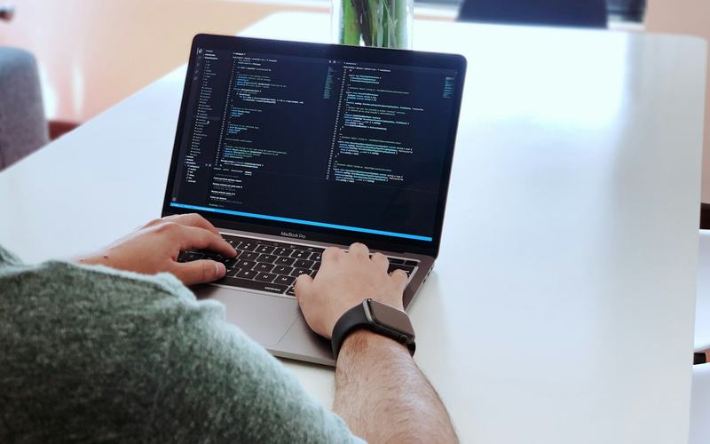 Iemand werkt aan code op een laptop aan een witte tafel.