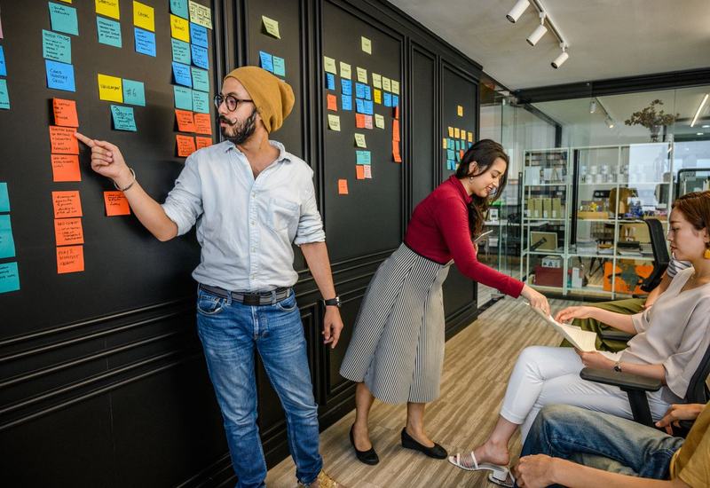 Een team bespreekt de planning aan een donkere wand vol post-its.