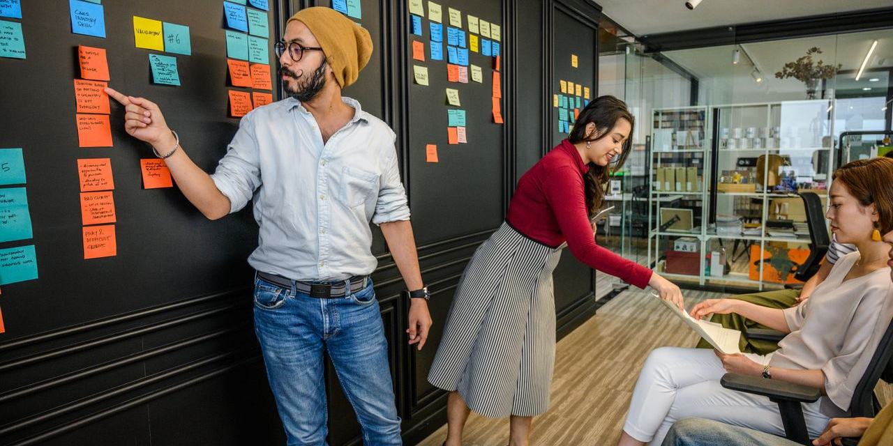 Een team bespreekt de planning aan een donkere wand vol post-its.