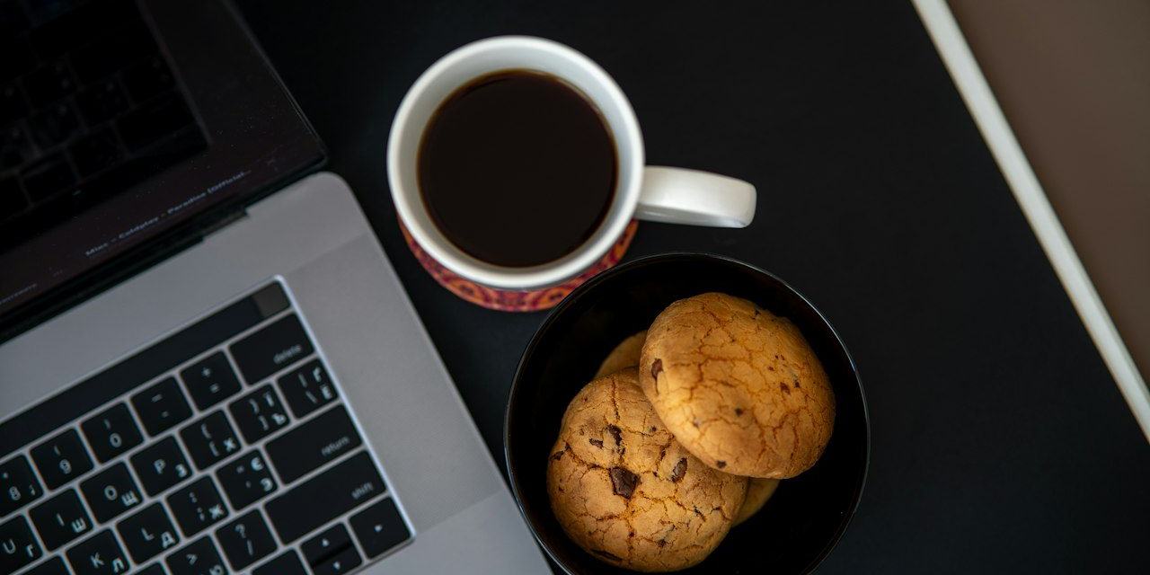 Een kop koffie en koekjes naast een laptop.