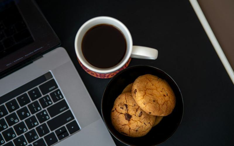 Een kop koffie en koekjes naast een laptop.