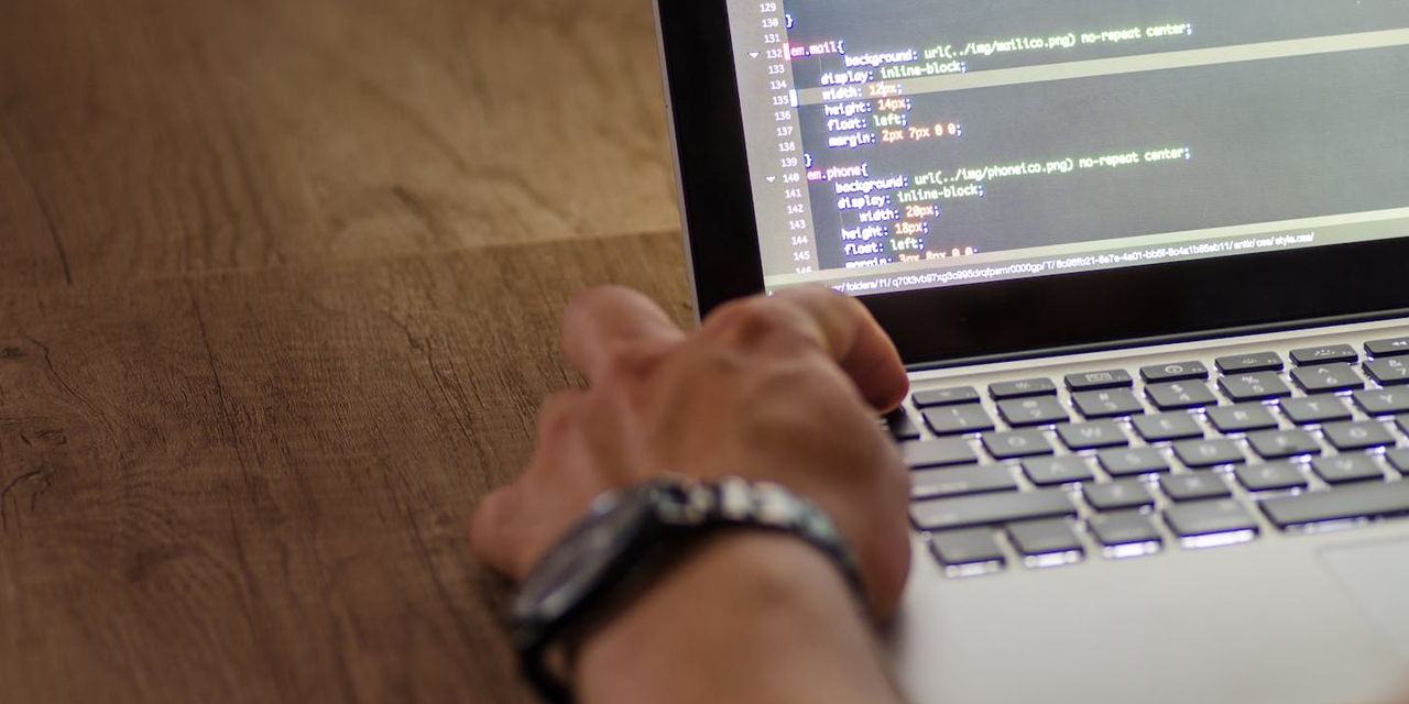 Een hand op het toetsenbord van een laptop, met code op het scherm.