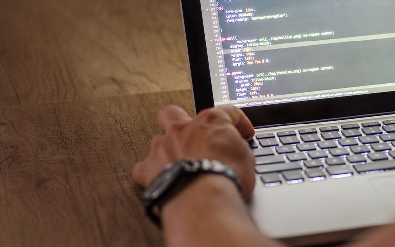Een hand op het toetsenbord van een laptop, met code op het scherm.
