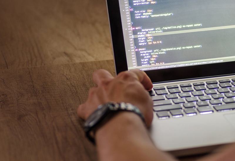 Een hand op het toetsenbord van een laptop, met code op het scherm.