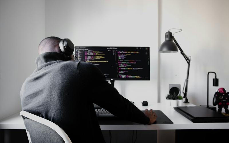 Een ontwikkelaar met een hoofdtelefoon kijkt naar code op een monitor.